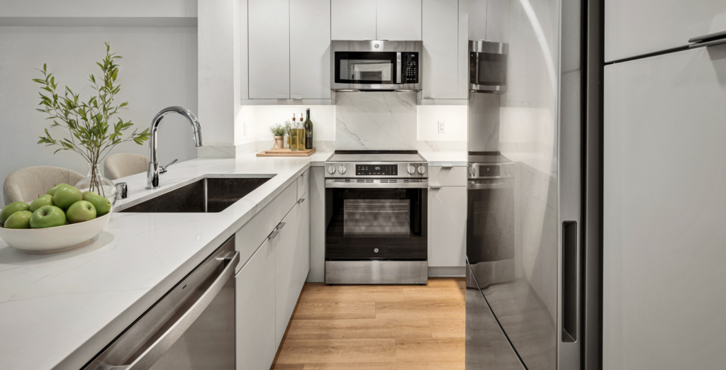 Modern white kitchen with stainless steel appliances, quartz countertops, and under-cabinet lighting.
