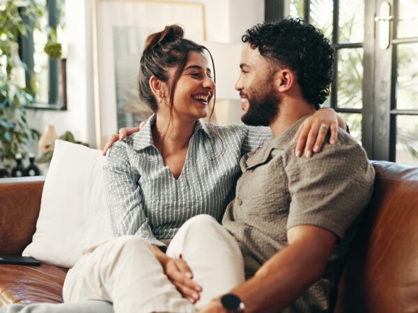 Couple smiling and embracing while sitting together on a couch in a bright, cozy living room.