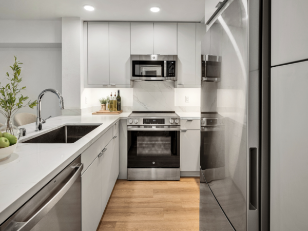 Modern white kitchen with stainless steel appliances, quartz countertops, and under-cabinet lighting.