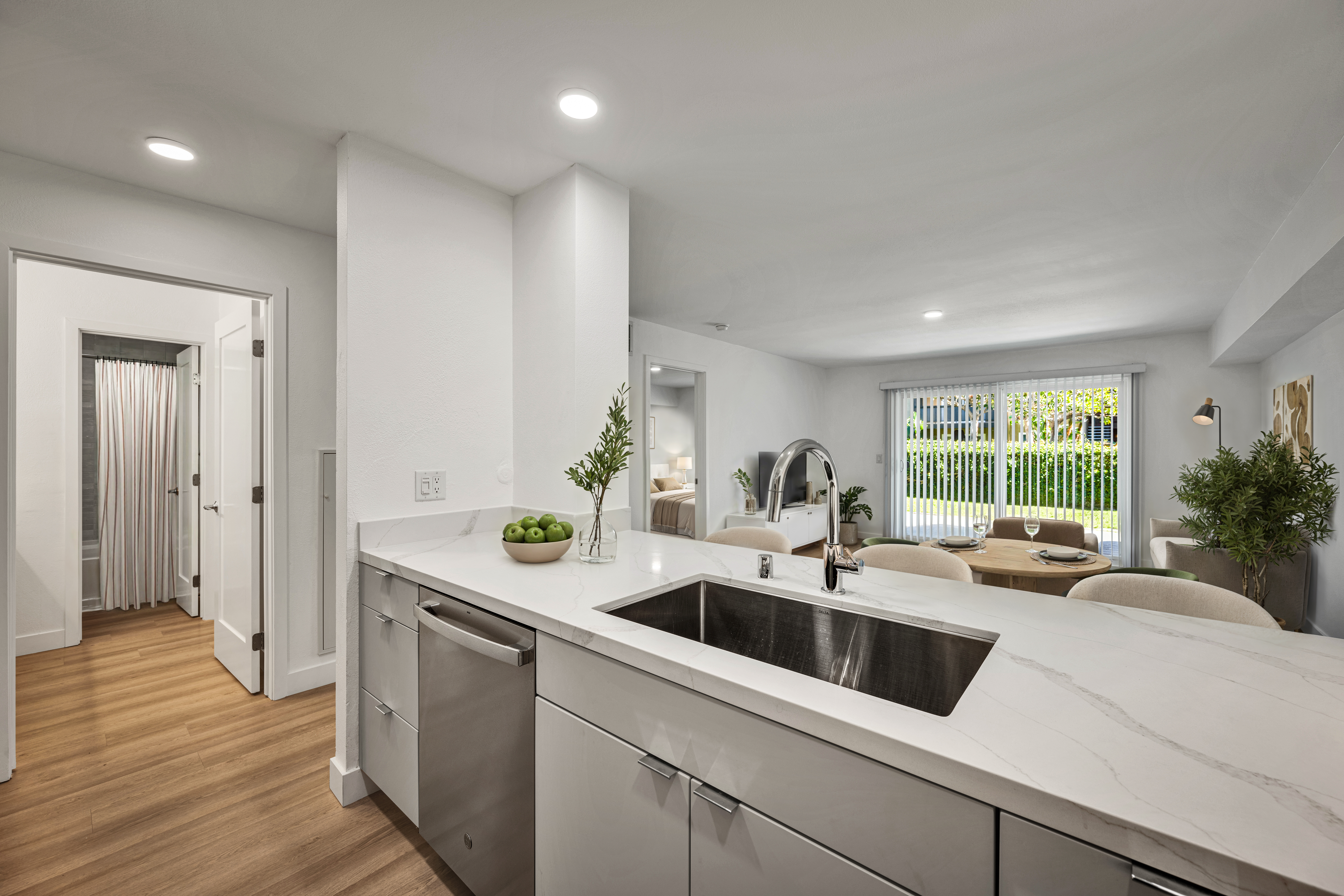 Open-concept kitchen with white countertops, wood cabinetry, stainless steel appliances, and living area beyond.