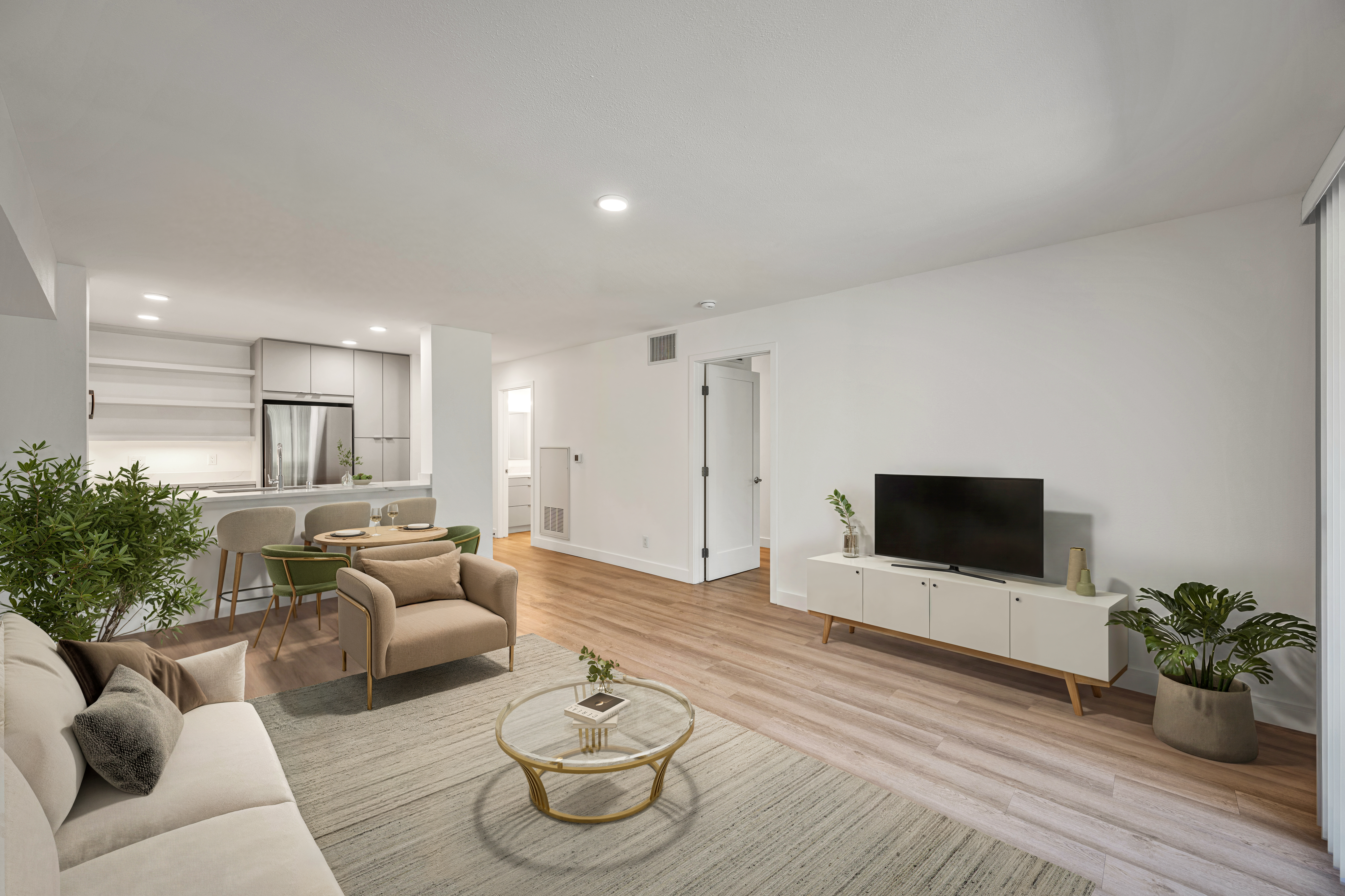 Bright open living room with sofa seating, TV console, dining area, and kitchen in the background.