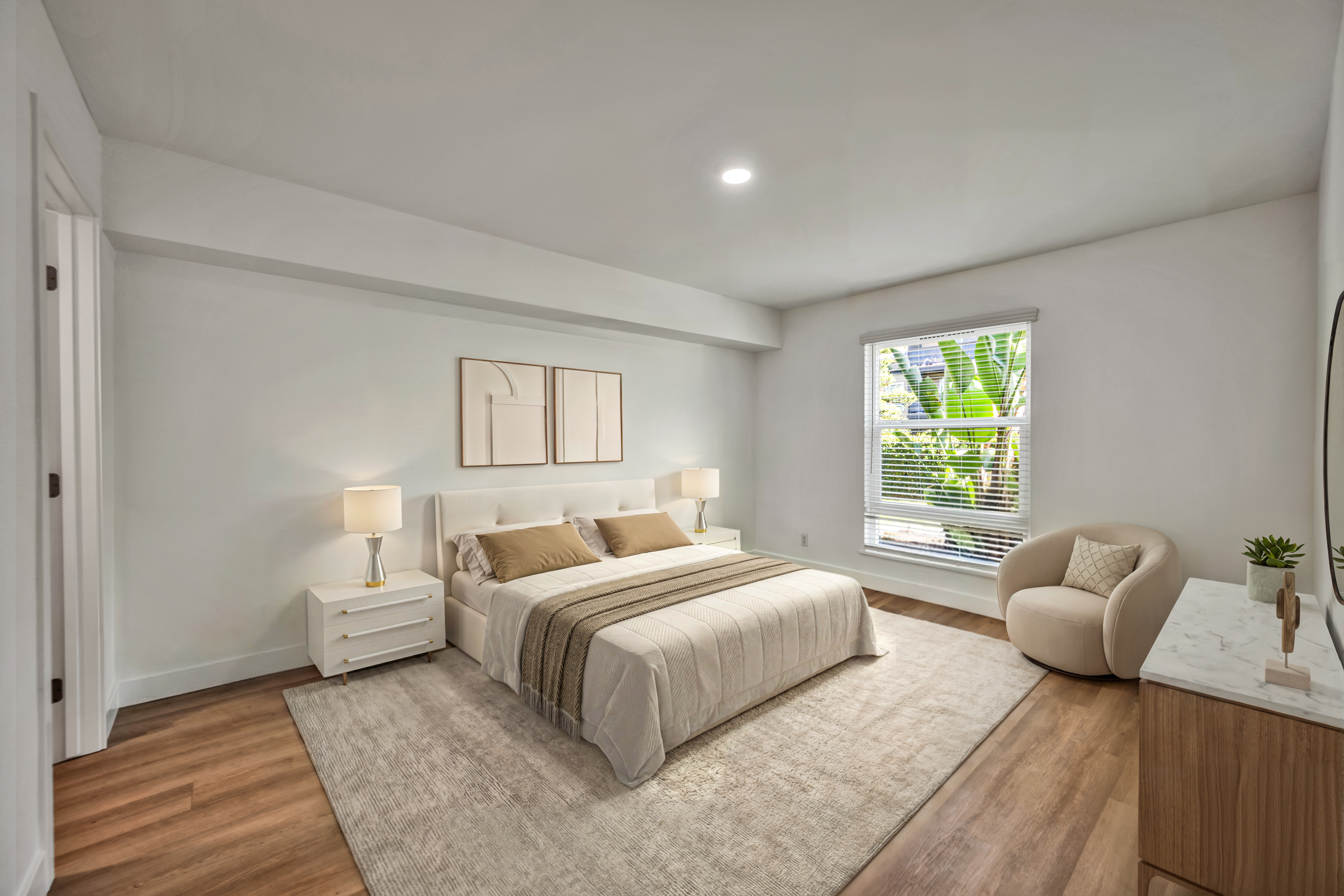 Bright bedroom with upholstered bed, nightstands, lamps, and large window overlooking greenery.