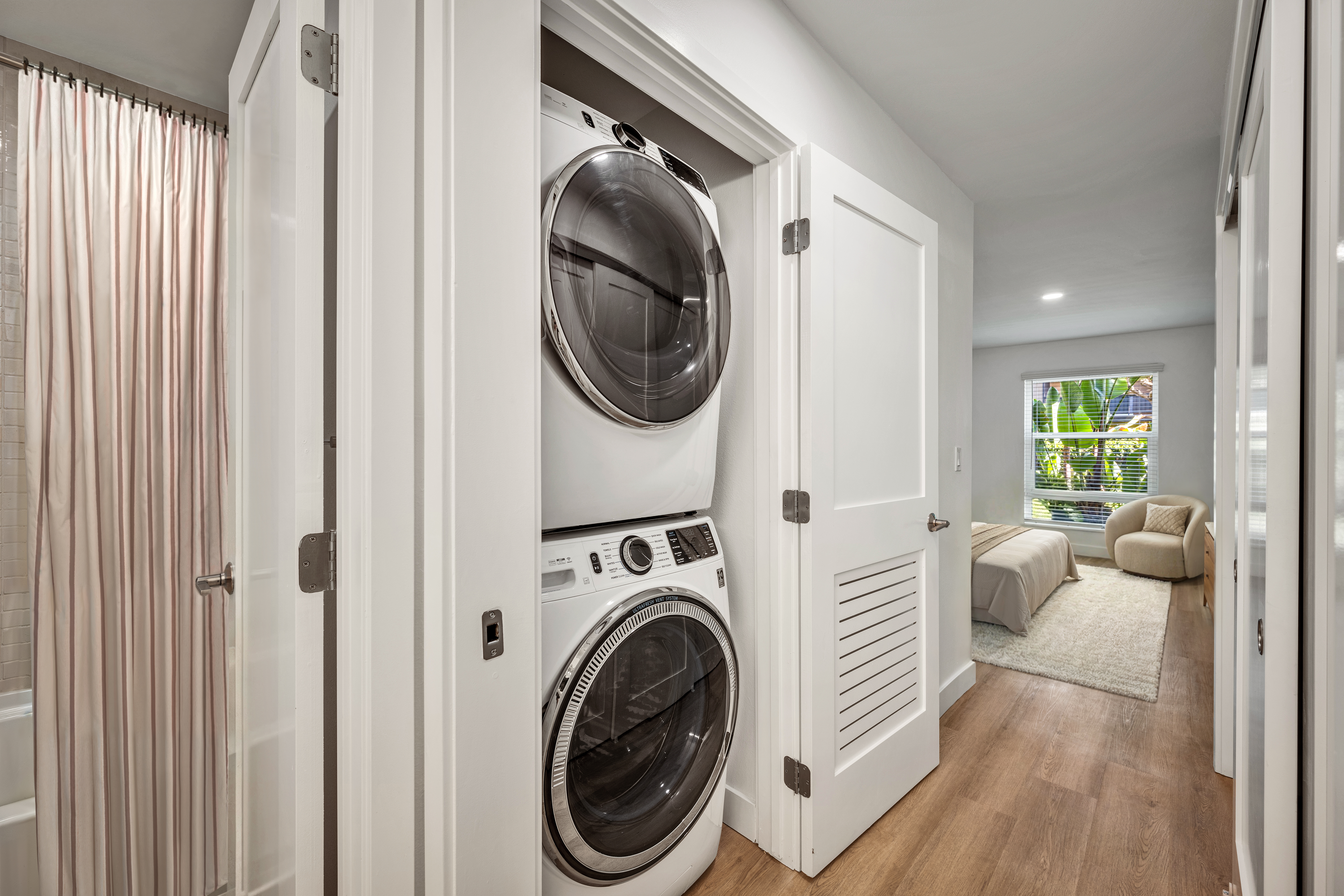 Hallway with stacked washer and dryer in a closet leading to a bedroom with large window.