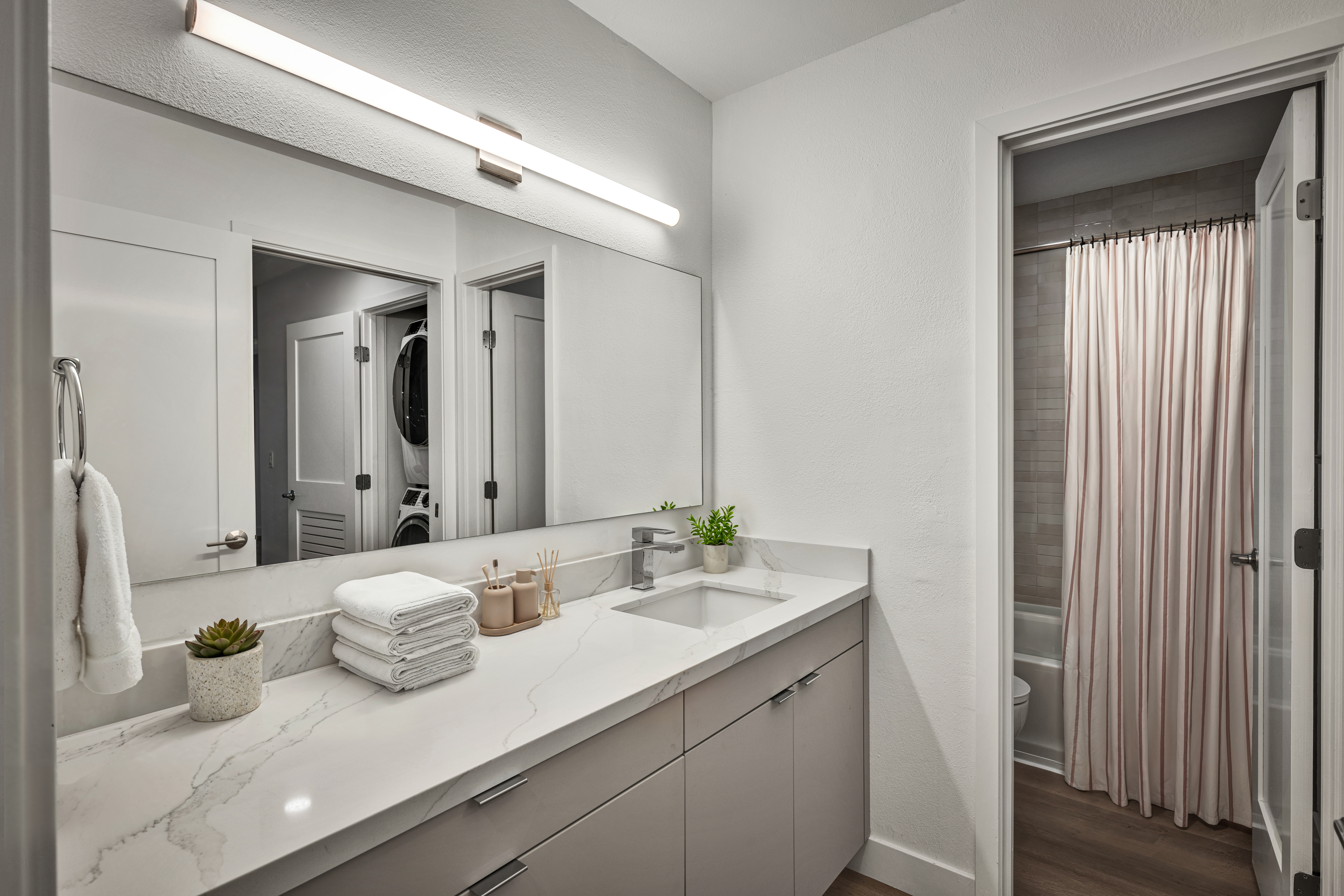 Modern bathroom with quartz vanity, large mirror, and adjacent shower with curtain.