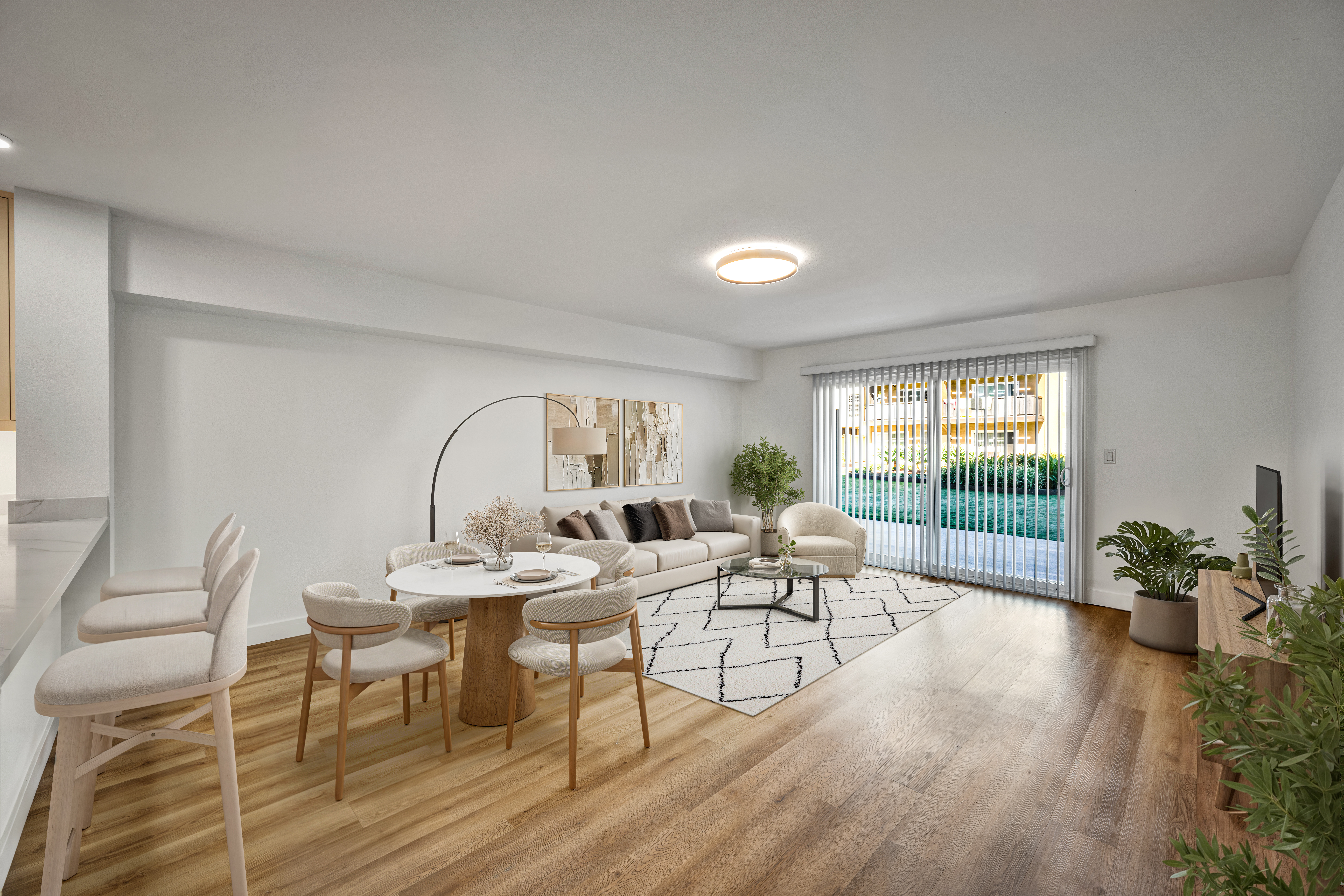 Bright modern apartment living and dining area with neutral furnishings, wood floors, and sliding glass doors to a patio.