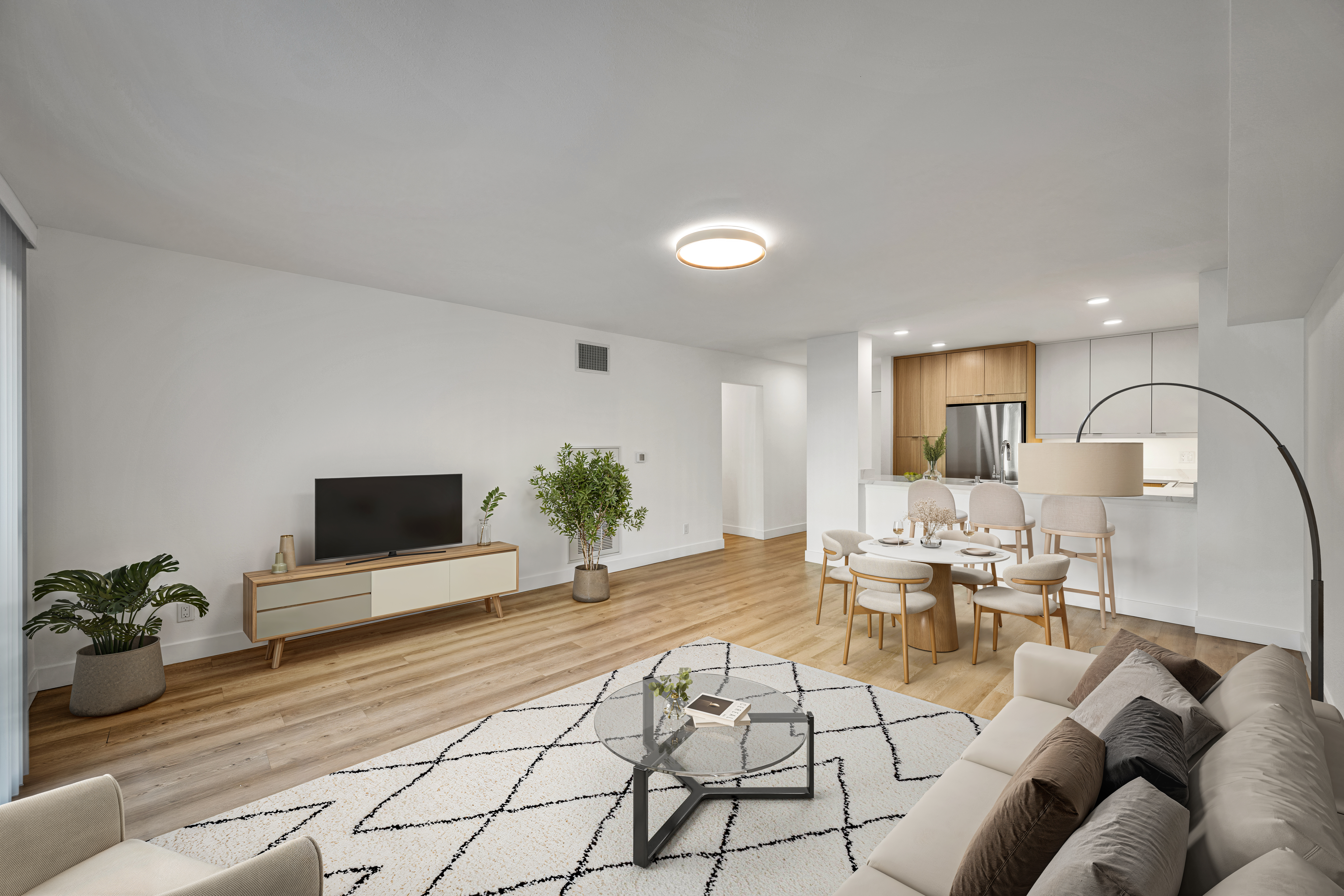 Open-concept living room and kitchen with dining table, TV console, light wood floors, and modern furnishings.